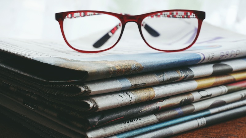 Red framed eyeglasses on top of pile of newspapers